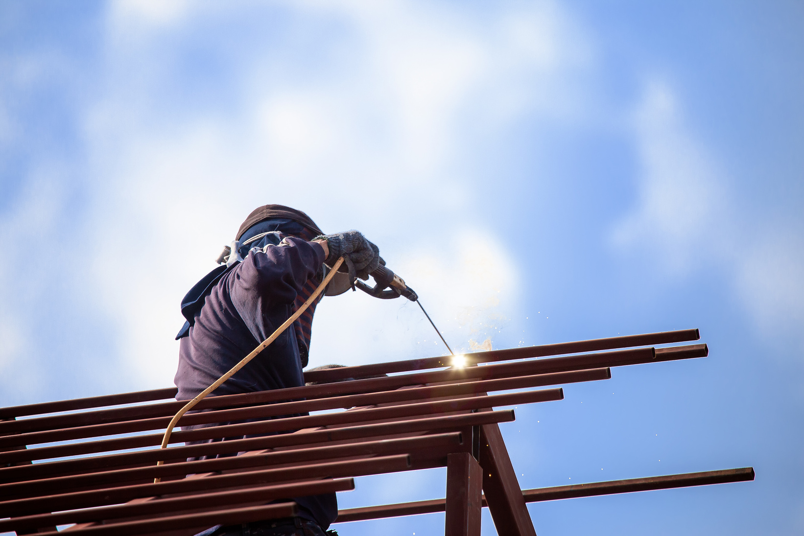 Red Painted Steel Roof Truss, with Roof Welders Working at Dange